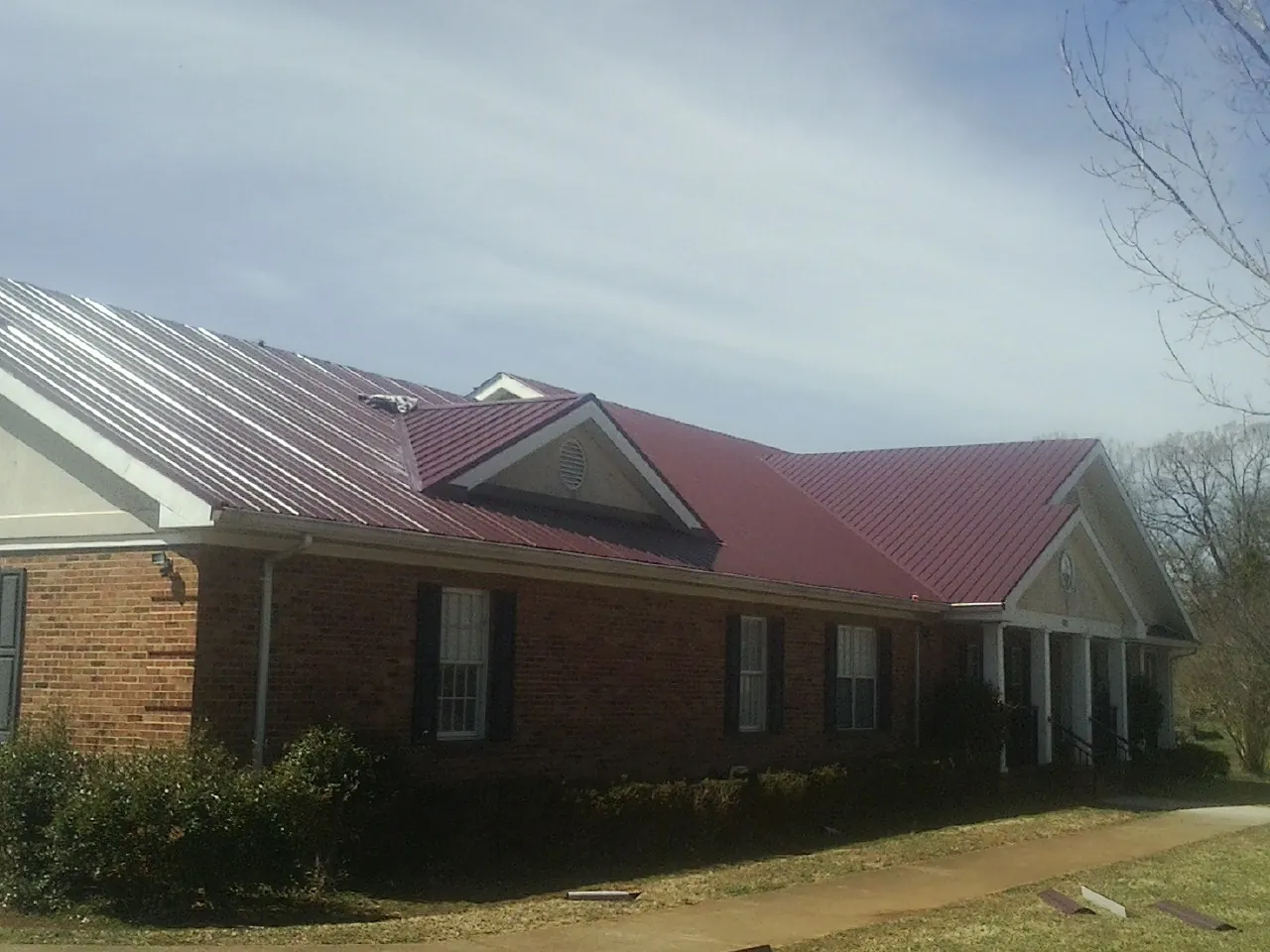Red metal roof with gabled entries on a long brick building, from a Hail Damage Roof Repair job in Walkersville